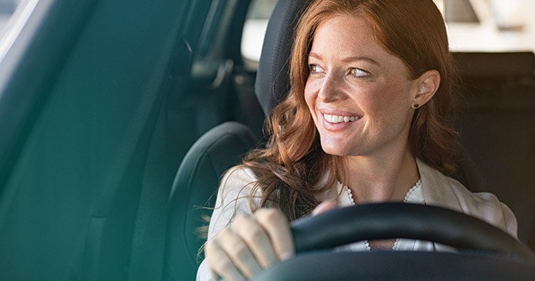 Happy woman behind car wheel